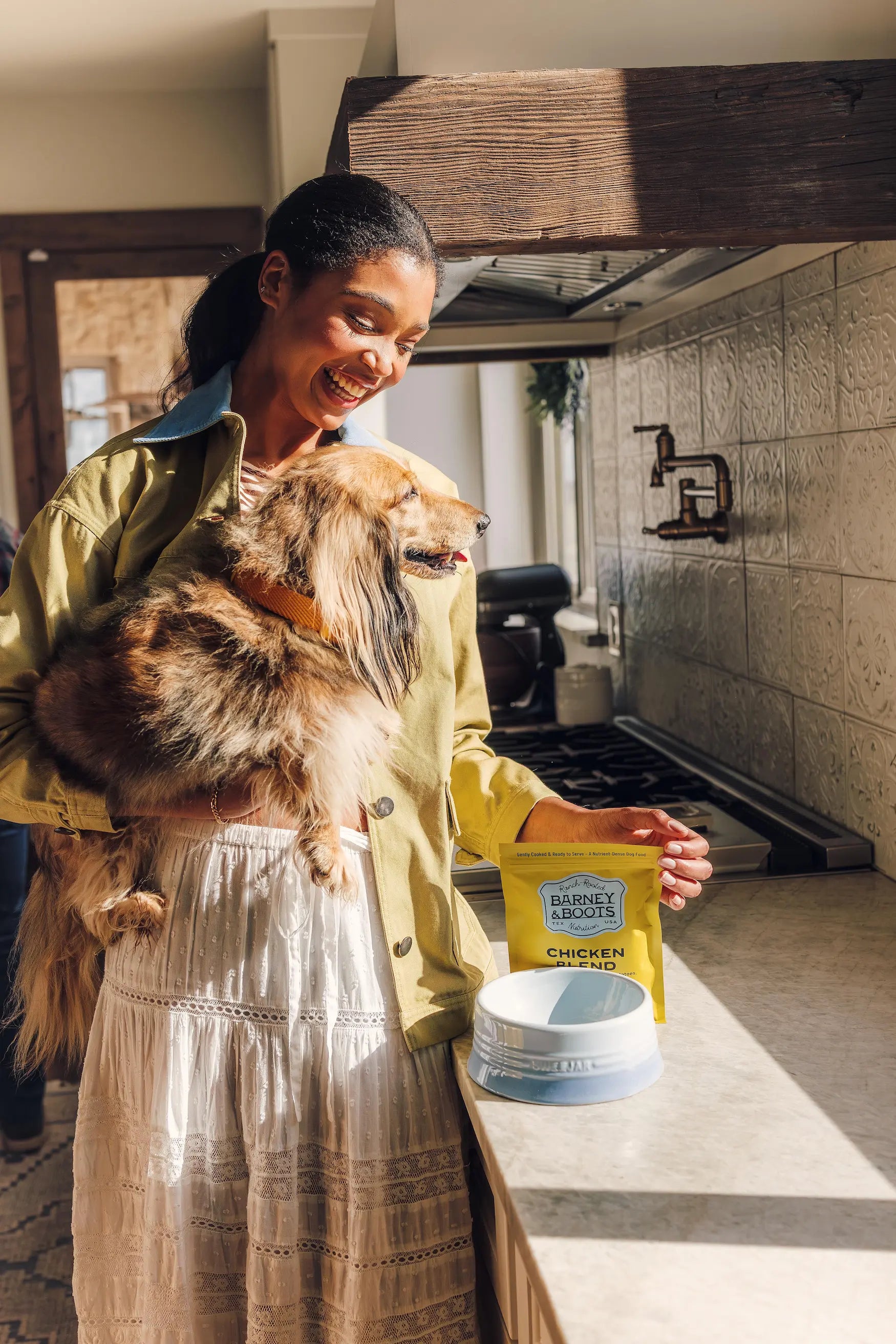 Woman holding her dog in the kitchen preparing Barney and Boots Chicken Blend dog food